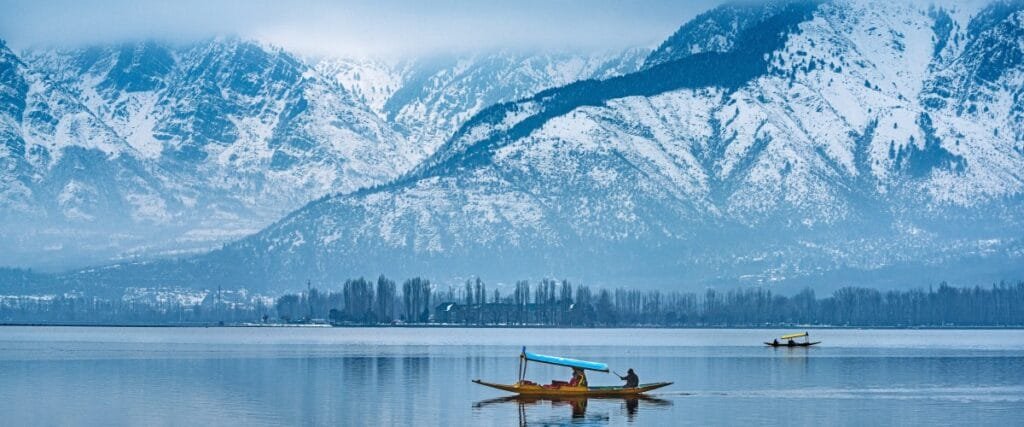 Shikara boat on Dal Lake with traditional houseboats and snow-capped Himalayan mountains during the Kashmir Highlights Tour covering Srinagar, Gulmarg, Pahalgam and Sonmarg.