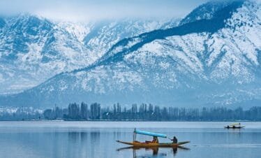 Shikara boat on Dal Lake with traditional houseboats and snow-capped Himalayan mountains during the Kashmir Highlights Tour covering Srinagar, Gulmarg, Pahalgam and Sonmarg.