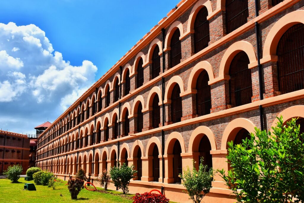 Panoramic view of Andaman's Cellular Jail, a three-story yellow colonial-era prison with seven wings radiating from a central tower under clear blue skies