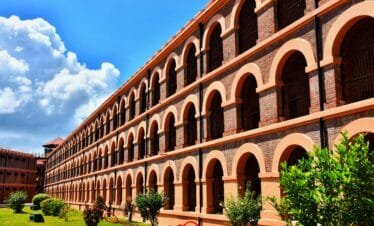 Panoramic view of Andaman's Cellular Jail, a three-story yellow colonial-era prison with seven wings radiating from a central tower under clear blue skies